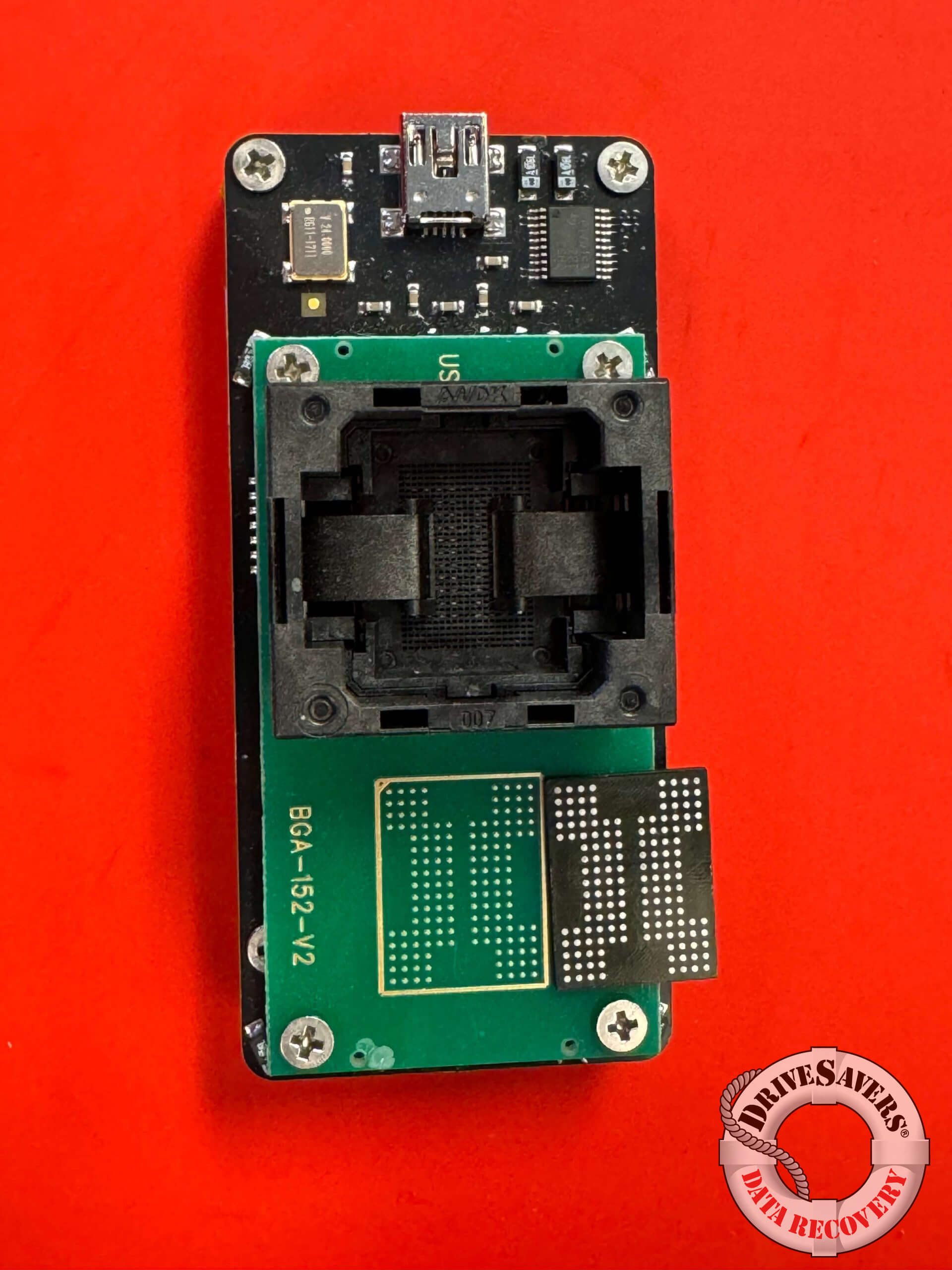 The image showcases a detailed close-up of a circuit board set against a red background. Prominently featured is a micro USB port alongside a central chip socket, surrounded by an array of intricate electronic components that form the device's architecture. The overall composition highlights the complexity and sophistication typical of modern electronic devices.