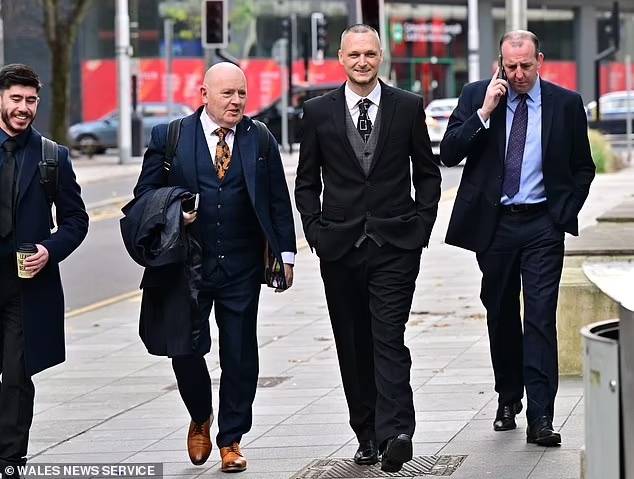 Four men in business attire walk along a city street. One is on a phone, likely discussing why his external hard drive keeps disconnecting, while another holds a coffee. They appear to be engaged in conversation, with buildings and traffic lights in the background.