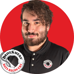 A person with curly hair and a beard is wearing a black polo shirt with a DriveSavers Data Recovery logo. The background is a solid red circle. The DriveSavers Data Recovery logo is also displayed in the bottom left corner.
